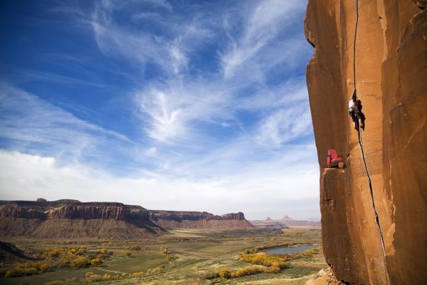 person climbs cliff with red movie theatre chair watching
