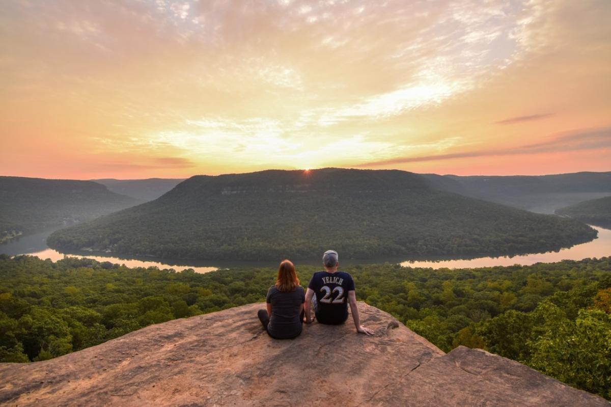 two people sit on Snooper's Rock looking out over view of river below them